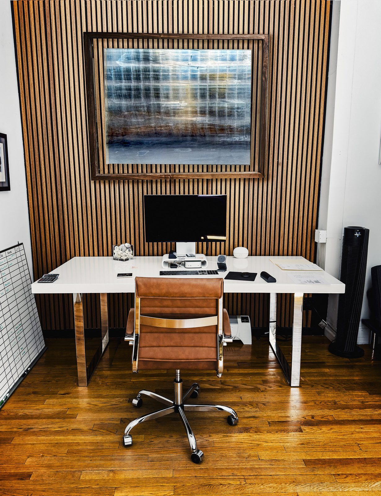 One of the works on a slatted wood wall above a writing desk and leather chair